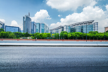 Empty asphalt road in the foreground with a view of modern glass office buildings and green trees...