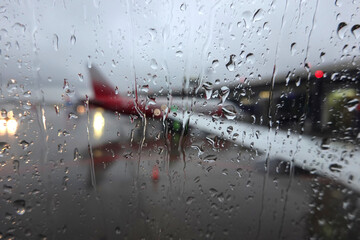 Blurred view to air field with aircrafts through wet glass in the overcast weather in the evening