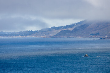 Fog rolling over the coastal hills near Point Sur, Big Sur, California. Scenic Pacific Ocean view with misty shoreline, rugged terrain, and iconic Highway 1 coastline landscape