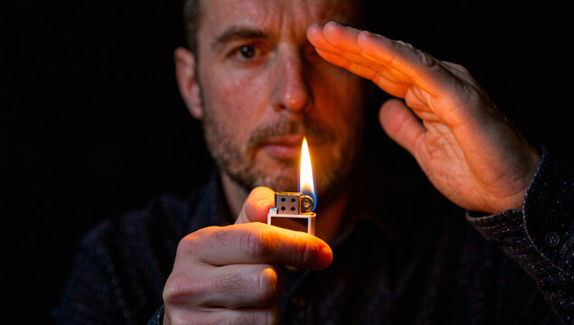 Man holding lit lighter and shielding eye with hand