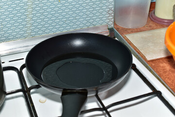 A top view of a frying pan placed on a gas stove with a flame lit in the burner.