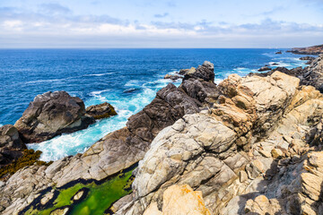 Dramatic Big Sur coastline along Highway 1, California. Waves crash against rugged cliffs, forming turquoise patterns in the Pacific Ocean, showcasing the raw beauty of the California coast