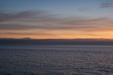 A hazy sky blending into clouds at the horizon during twilight over a serene sea with gentle waves.
