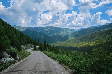 Curving asphalt highway through summer mountains under a partly cloudy sky