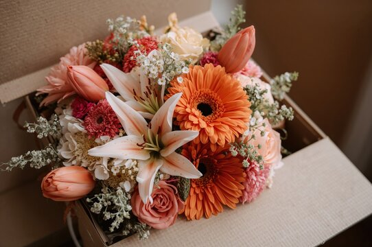 Bouquet of orange roses, lilies, gerberas, tulips, and assorted summer blooms in a brown box prepared for delivery at a wedding