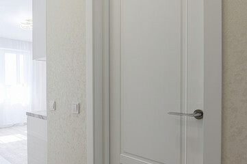 bright shot shows a white door with a chrome handle, framed by a light-colored wall with switches. In the background, a glimpse of a bright, modern room