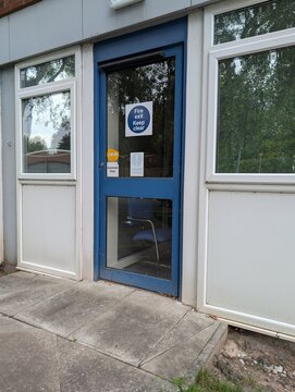 Blue office exterior door marked with a fire exit sign that has a chair on the inside blocking the safe exit route in the case of a fire breaching all health and safety laws and fire regulations.