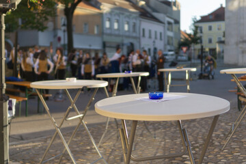Low angle close up of white metal cafe tables with blurred background of a traditional brass band performing in a quaint european town a festival, celebration event concept of tourism agency