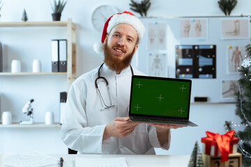 Doctor on the shift showing green screen chroma key monitor with space to advertisement in hospital at christmas eve