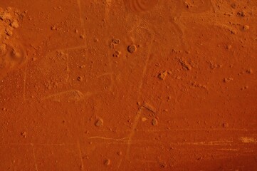 Empty outdoor clay tennis court with light orange surface and gravel texture, showing baseline and net on a sunny day with yellow-green ball, dry grungy ground details, ample copy space