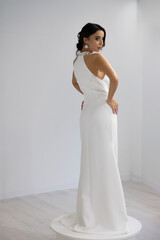 Stylish woman in white long dress posing with elegance in minimal bright studio