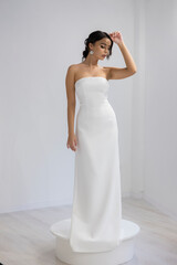 Fashion model in long strapless white dress posing gracefully in studio