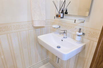 Fototapeta premium clean, well-lit bathroom corner features a white sink with chrome fixtures, neutral-toned tiles, decorative elements on a shelf and towel rack