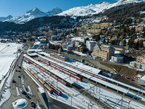 Aerial view of the red trains lined up at the Filisur train station against a backdrop of snow-covered mountains and charming buildings, St moritz, Switzerland.