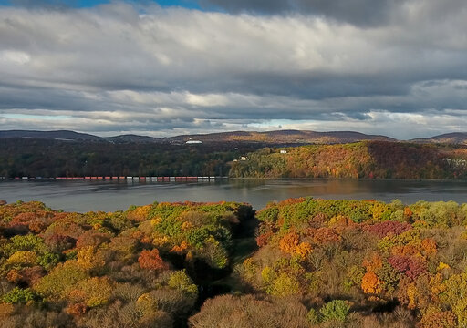 Aerial view of a river cutting through forests painted in hues of autumn, with a bridge gracefully arching over the water, Hudson River