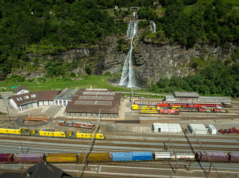 Aerial view of trains nestled in the valley near the cascading waterfall, the buildings with brown roofs and green trees adding a vibrant touch, Filisur, Switzerland.