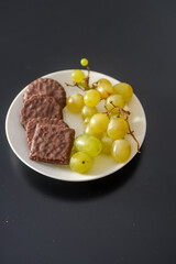 White grapes and chocolate biscuits on the same plate as two contrasts of healthy and unhealthy sugars and so-called treat foods on a dark background