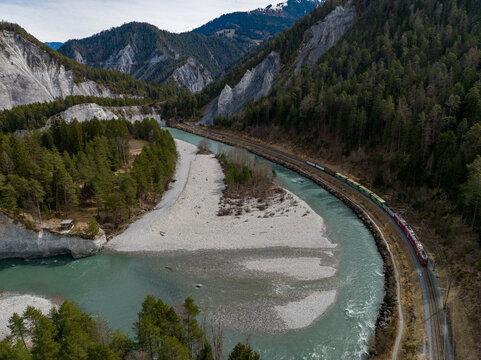 Aerial view of the turquoise Rhine carves its way through the rugged mountains, a railway hugging its edge near the dramatic rock formations, Rhine River, Switzerland.