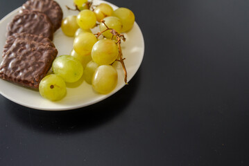 White grapes and chocolate biscuits on the same plate as two contrasts of healthy and unhealthy sugars and so-called treat foods on a dark background