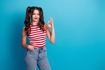 Young woman in striped top making hand gesture for OK sign with confident expression, posing...