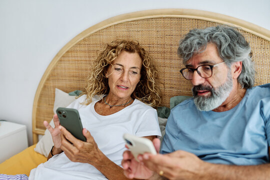 Senior middle aged couple using phone in bed in bedroom - Powered by Adobe