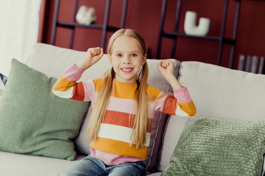 Fototapeta Young daughter joyfully spending time at home on a comfy sofa, enjoying fun moments in a cozy living room environment