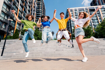 Group of cheerful young friends jumping outdoors in the city celebrating together on a sunny day