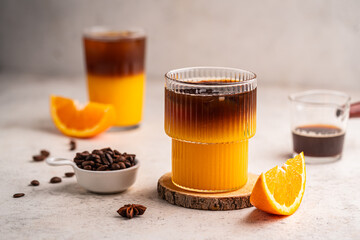 Coffee with orange juice (bumble) in a tall glass with ice on a light background with coffee beans...