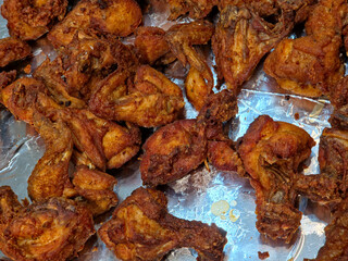 Large pile of deep-fried chicken pieces, primarily consisting of wings and various small cuts  displayed on a tray lined with reflective aluminum foil.