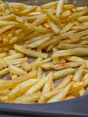 A large pile of classic-cut french fries filling a metal catering pan, verticle image.