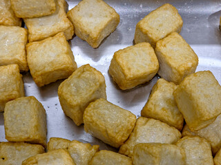 Scattered pile of fish tofu cubes resting in a stainless steel tray or pan. 