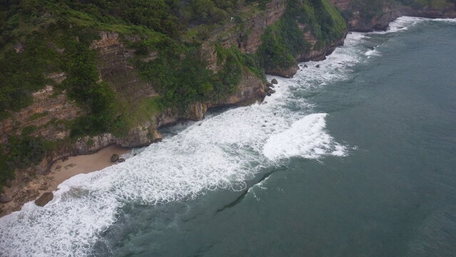 Title
Aerial View of Tropical Beach with Waves Crashing on Shore and Green Cliffs

Description
Scenic aerial view of a tropical coastline with waves hitting sandy beach and lush green cliffs, natural 