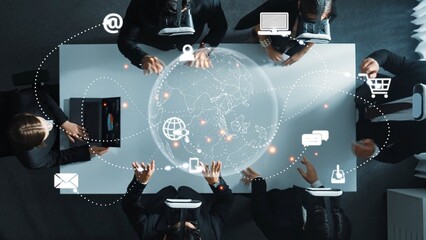 A professional business team collaborates on innovative ideas over a table with digital interfaces, communication symbols, and global connectivity concepts showcased. Raster