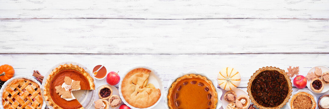 Homemade fall pie bottom border. Top view on a white wood banner background with copy space. Assortment of apple, pumpkin and pecan pies.