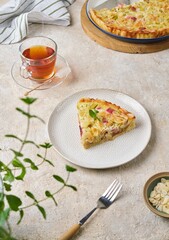 Sliced ​​shortcrust pastry tart with rhubarb, plum jam, and almonds on a plate against a light concrete background.
