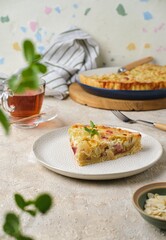Sliced ​​shortcrust pastry tart with rhubarb, plum jam, and almonds on a plate against a light concrete background.