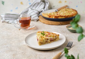 Sliced ​​shortcrust pastry tart with rhubarb, plum jam, and almonds on a plate against a light concrete background.