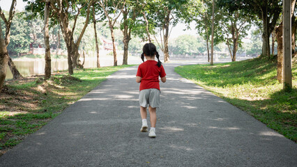 Fototapeta premium Young child walking alone on a peaceful pathway surrounded by trees in a serene park setting enjoying nature and fresh air on a sunny day