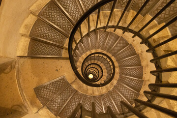 Fototapeta premium Spiral staircase viewed from above, showcasing intricate metal railings and textured steps, creating a captivating architectural design with depth and perspective