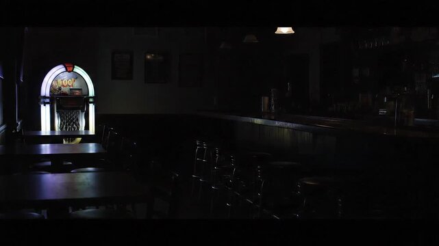 Retro jukebox glows in dimly lit bar, evoking nostalgia and quiet anticipation for music and patrons.