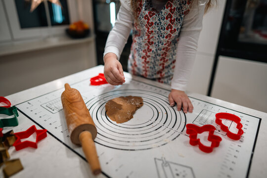 A delighted child bakes cookies with a rolling pin and colorful cutters in a warm, festive holiday kitchen
