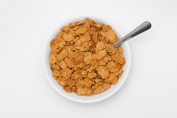 Overhead view of bran flakes cereal in a bowl with a spoon. Healthy breakfast food high in fiber and nutrition, ideal for diet, organic lifestyle, and wholesome morning meals.