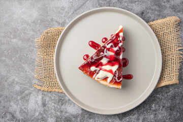 Cheesecake slice with fruit sauce and glaze on ceramic plate over burlap, top view food photography for dessert presentation and culinary design