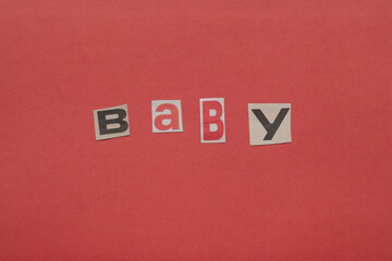 Baby word forming ransom note style message on red surface