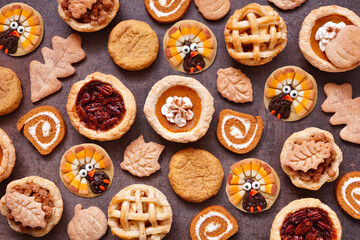 Thanksgiving or autumn dessert background. Top view against a dark background. Pumpkin, apple and pecan mini pies, turkey, leaf and snickerdoodle cookies, pumpkin rolls.
