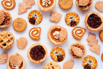 Thanksgiving or autumn dessert background. Top down view against white marble. Pumpkin, apple and pecan mini pies, turkey, leaf and snickerdoodle cookies, pumpkin rolls.