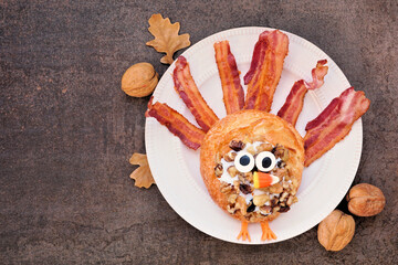 Fun Thanksgiving turkey breakfast pastry with bacon. Top down view table scene against a dark background.