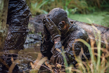 soldier in the swamp's muddy water swipes off the mud of his face