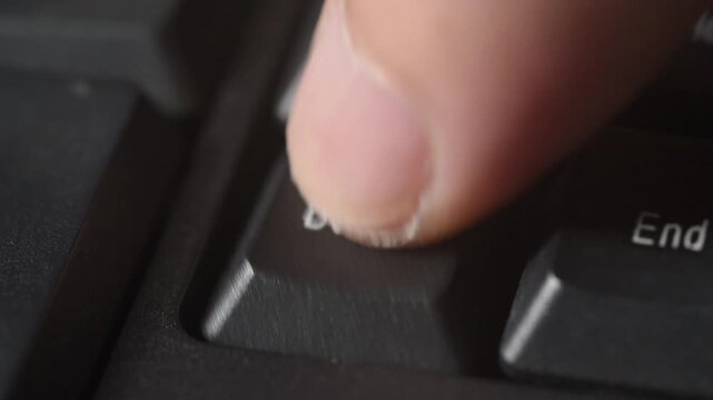 Finger presses delete key on black keyboard symbolizing digital termination and control in computer technology input and data management tasks