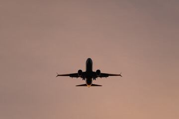 Symmetrical silhouette of a commercial jetliner on approach, with sunset light glowing on its engines and tail.